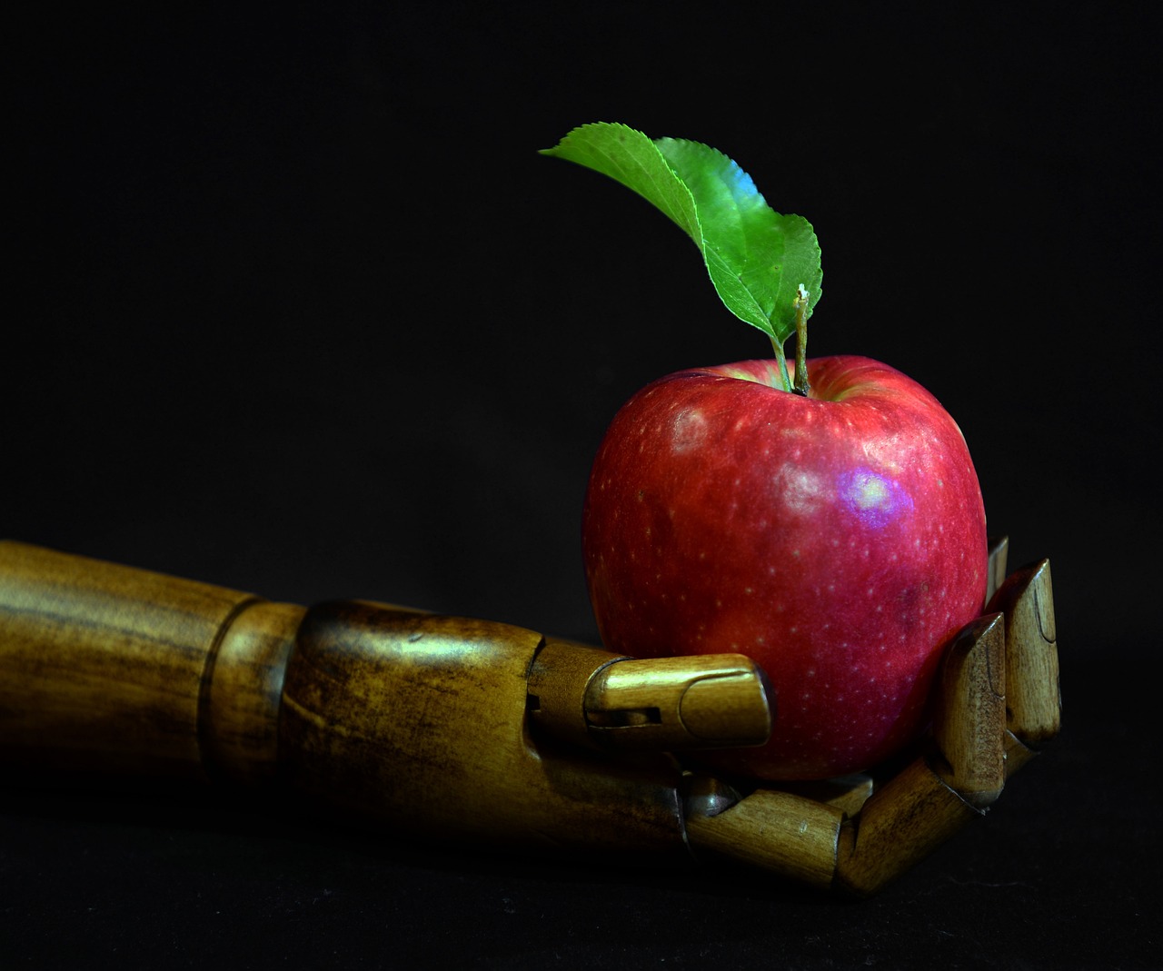 Golden robotic hand holding a red apple with green leaf