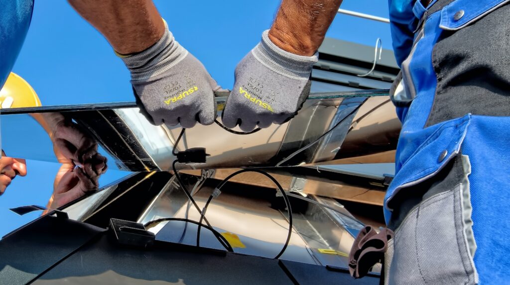 Photo of close up of hands of two men carrying a metal sheet as they install solar panels
