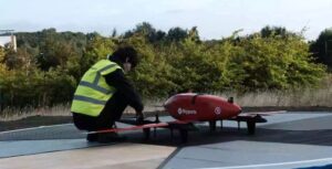 A researcher in a high-visibility jilet attends a red UAV drone being tested as part of Project CAELUS