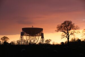 Sunset silhouettes a giant radio telescope and trees